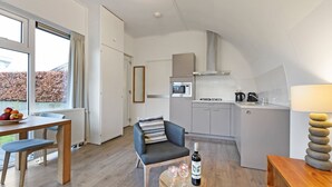 Une cuisine moderne équipée d’un four à micro-ondes, d’une cuisinière et d’une machine à café. On y trouve un coin repas avec une table et des chaises, ainsi qu’un canapé avec un coussin. Une bouteille de vin et des verres sont posés sur une petite table.