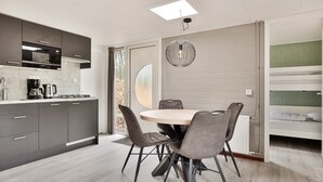 Une cuisine moderne avec des armoires grises, un four encastré et une machine à café. On y trouve un coin repas avec une table ronde et quatre chaises. Une grande fenêtre offre une lumière naturelle et une vue sur l’extérieur.