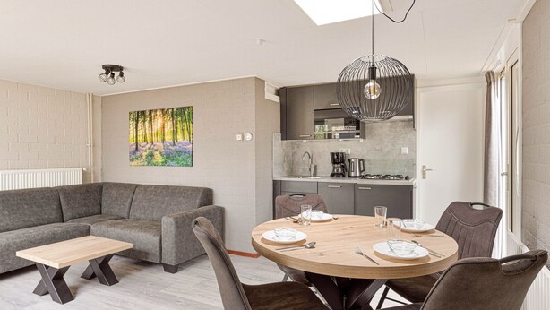 Un salon moderne avec un canapé gris, une table basse en bois et une table à manger pour quatre personnes.