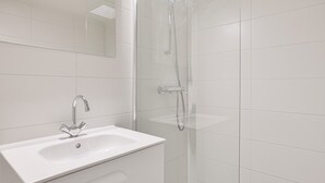 Une salle de bain moderne avec un lavabo blanc, un miroir et une douche séparée par une paroi de verre.