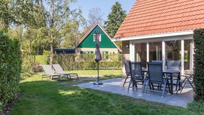 Un patio con mobiliario exterior, una casa de jardín al fondo y un jardín bien cuidado.