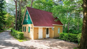 Una pequeña casa de madera de un solo piso con techo rojo, rodeada de abundante vegetación y árboles.