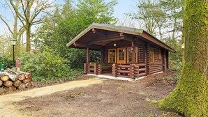 Eine rustikale Blockhütte mit Veranda, umgeben von dichtem Grün und Bäumen.