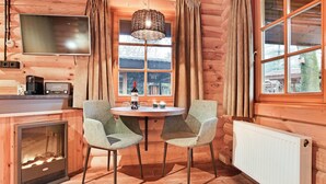 Ein gemütliches Blockhaushaus-Interieur mit Holzvertäfelung, einem Esstisch mit Stühlen, einem Fernseher und einem Kamin.