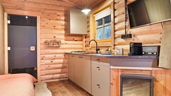 A compact log cabin room with a kitchenette, a bed, and a window with a view.