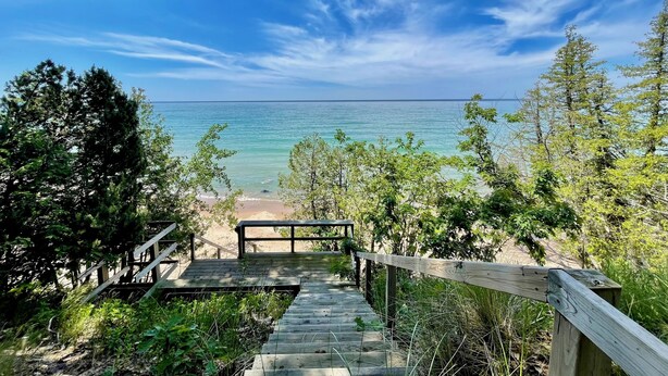 A wooden staircase leading to a beach with clear blue water and a view of the ocean.