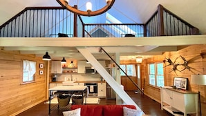 A spacious loft-style living area with a red sofa, a staircase leading to an upper level, and a kitchen in the background.