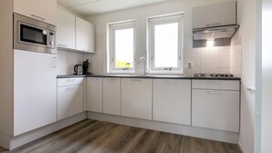 A modern kitchen with white cabinets, a microwave, a coffee maker, and a gas stove. - Detached bungalow for 6 persons (Tynaarloo)
