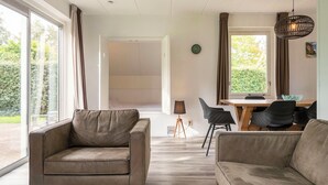 A modern living room with a sofa, a dining table with chairs, and a large window with curtains. - Detached bungalow for 6 persons (Tynaarloo)