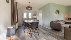 A modern kitchen with a dining table and chairs, a sofa, and a pendant light. - Detached bungalow for 6 persons (Tynaarloo)