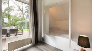 A room with a bed, a window with curtains, a table with chairs, and a lamp. - Detached bungalow for 6 persons (Tynaarloo)