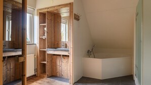 Een moderne badkamer met een houten wastafelmeubel, een vrijstaand bad en een raam dat voor daglicht zorgt.