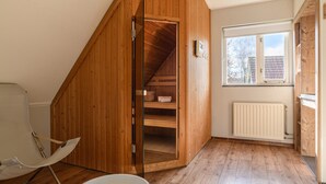 Een slaapkamer met een zolderkamer, schuine wanden, een raam met uitzicht op bomen en een radiator.