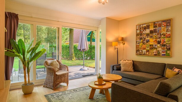 Een gezellige woonkamer met een bank, een rieten fauteuil, een klein tafeltje en een potplant.