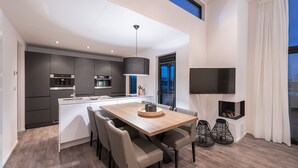 Une cuisine moderne avec des meubles de couleur sombre, un îlot central et un coin repas comprenant une table et des chaises en bois.