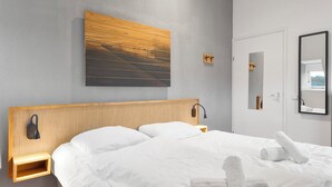 A hotel room with a wooden headboard, a large painting of a sunset, a bedside table with a lamp, and a mirror on the wall. - Comfortable bungalow for 6 persons (Midlaren)