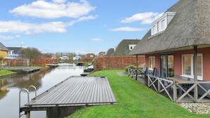 A riverside property with a wooden deck, a thatched-roof building, and a canal. - Comfortable bungalow for 6 persons (Midlaren)