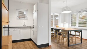 A modern kitchen with white cabinets, a black countertop, and a wooden floor. There is a dining area with a table and chairs. - Comfortable bungalow for 6 persons (Midlaren)