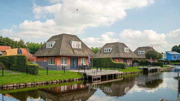 A row of traditional thatched-roof cottages with a water canal in the foreground. - Comfortable bungalow for 6 persons (Midlaren)