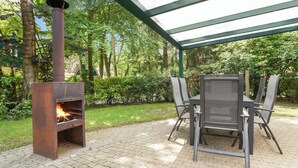 An outdoor patio with a metal grill and a table with chairs. - Comfortable bungalow for 6 people (Diessen-Baarschot)