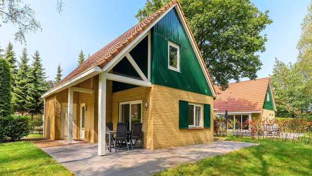 A two-story house with a green facade and a red-tiled roof. It has a covered patio with outdoor furniture. - Comfortable bungalow for 4 persons (Diessen)