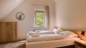 A bedroom with a bed, a wooden wardrobe, a window with curtains, and a round mirror on the wall. - Comfortable bungalow for 4 persons (Diessen)