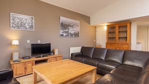 A living room with a leather sofa, a wooden coffee table, a TV, and two framed pictures on the wall.