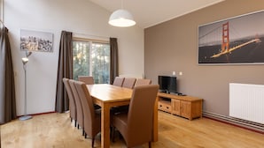 A dining area with a wooden table and chairs, a television on a wooden cabinet, and a cityscape painting on the wall.