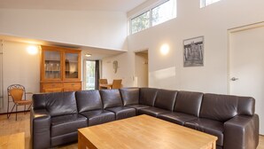 A living room with a large leather sectional sofa, a wooden coffee table, and a dining area with wicker chairs.
