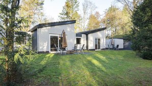 A modern two-story house with a patio area featuring outdoor furniture and a large umbrella.
