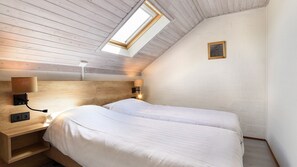 A room with a sloped ceiling, a skylight, a bed with two pillows, a bedside table with a lamp, and a small framed picture on the wall. - Detached 4-person bungalow (Vijlen)