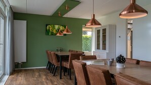 A dining area with a green wall, wooden table, brown chairs, and copper pendant lights. - Bungalow Wellness 14 (Vlagtwedde)