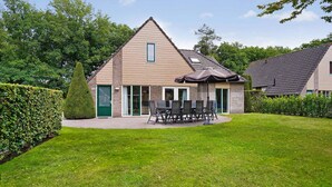 Une maison à deux étages avec un toit en pente, une terrasse dotée de mobilier d’extérieur et une pelouse bien entretenue.
