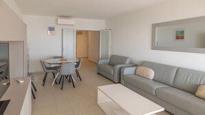 Un saló modern amb un sofà, una taula de centre, una taula de menjador amb cadires i una televisió.