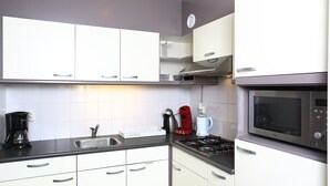 A kitchen with white cabinets, a gas stove, a microwave, a coffee maker, and a kettle. - Comfortable detached or semi-detached bungalow for 6 persons (Vlagtwedde)