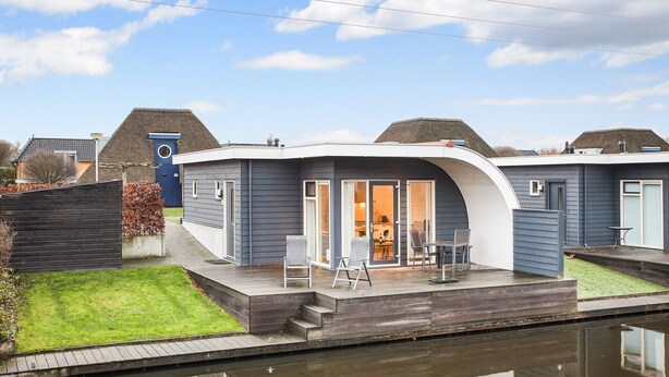 Ein modernes Haus mit gewölbtem Dach, einer kleinen Terrasse mit Sitzgelegenheit und einem sichtbaren Küchenbereich.