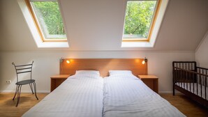 Une chambre à coucher avec un grand lit, deux tables de chevet, une tête de lit en bois, une chaise et deux fenêtres de toit.