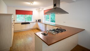 Une cuisine moderne avec des meubles blancs, un îlot central doté d’une cuisinière à gaz et deux fenêtres équipées de stores rouges.