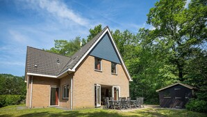 Une maison à deux étages, avec un toit en pente, une façade en briques et un petit garage attenant.