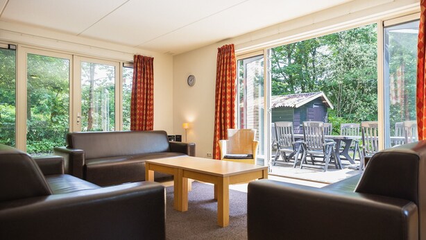Une pièce confortable avec un canapé, des fauteuils, une table et de grandes fenêtres donnant sur l’extérieur.
