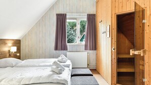 Ein Schlafzimmer mit einem Bett, zwei Kissen, einem Nachttisch mit Lampe, einem Fenster mit Vorhängen und einer Holztür.