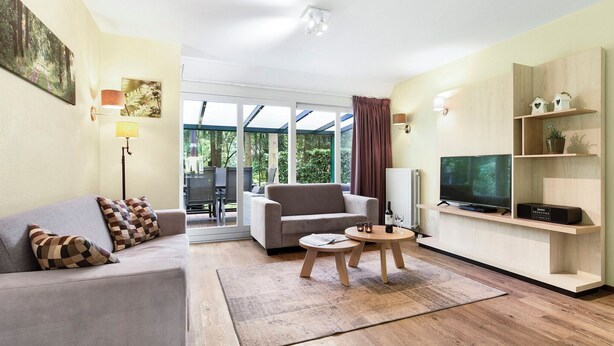 Ein modernes Wohnzimmer mit Sofa, Sessel, Fernseher und Regalen.