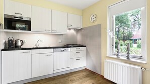 Eine moderne Küche mit weißen Schränken, einer schwarzen Arbeitsplatte, einem eingebauten Backofen und einem Fenster mit Blick ins Grüne.