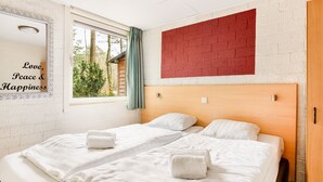 Habitación de hotel con dos camas, una pared de acento roja, un ventanal con vistas a árboles y un espejo con una frase motivacional.
