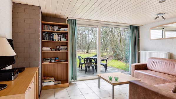 Un salon comprenant un canapé, une table basse, une bibliothèque et une porte-fenêtre coulissante donnant sur un espace extérieur aménagé avec des chaises.