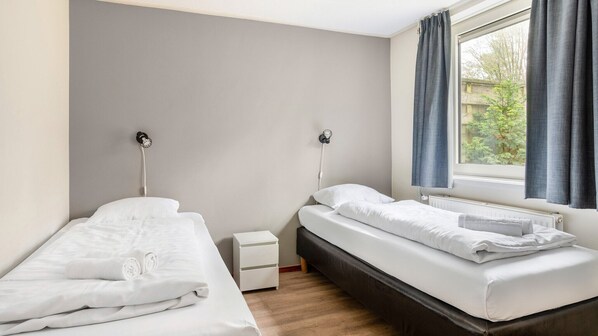 Un dormitorio con dos camas individuales, una mesita de noche pequeña y una ventana con cortinas.