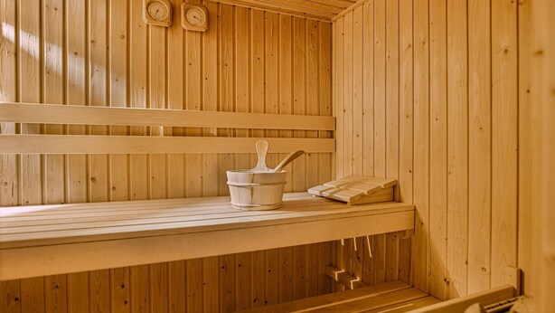 Una sauna de madera con bancos, un cubo de madera y un perchero para toallas.