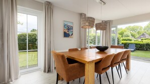 A spacious dining area with a wooden table and brown chairs, large windows with curtains, and a hanging light fixture.