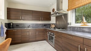 A modern kitchen with dark wooden cabinets, a stainless steel range hood, and a window with a view of greenery.