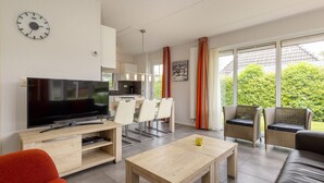 A modern living room with a flat-screen TV, a wooden coffee table, and a dining area with white chairs.